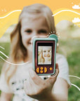 A young girl holds a teal and maroon digital camera, displaying her smiling reflection.