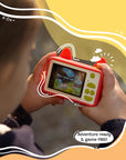 Child holding Kidamento Model C Fox camera showing back screen with fun message and kid-friendly buttons