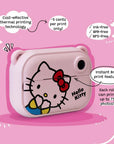 Side angle view of the kiimento Hello Kitty Model P kids digital camera showing its instant black-and-white thermal print feature. Highlights include cost-effective printing at approximately 5 cents per print, using ink-free, BPA-free, and BPS-free technology. Features Hello Kitty’s face on a pink camera body.