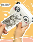 Hands holding Kidamento Model P Panda camera printing a black and white photo instantly, with playful orange background.
