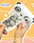 Hands holding kiimento Model P Panda camera printing a black and white photo instantly, with playful orange background.