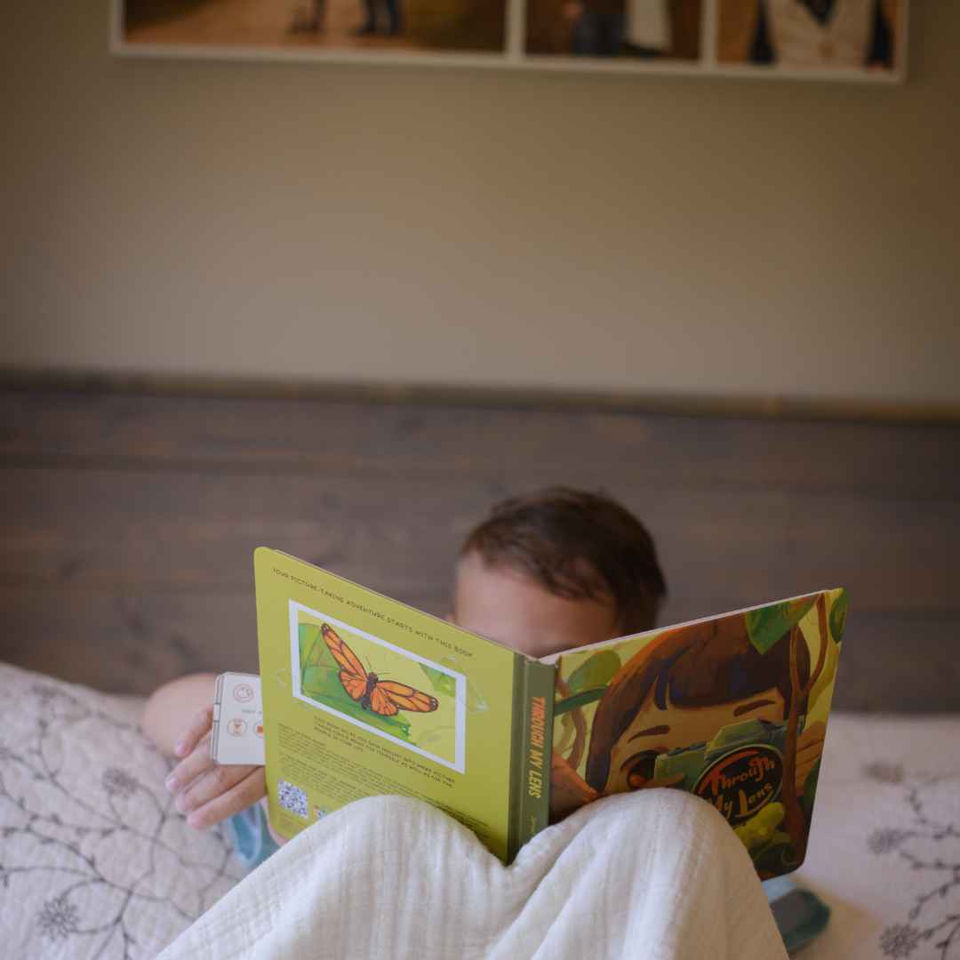 A child reads an open activity book titled &quot;Through My Lens&quot; with a butterfly illustration.