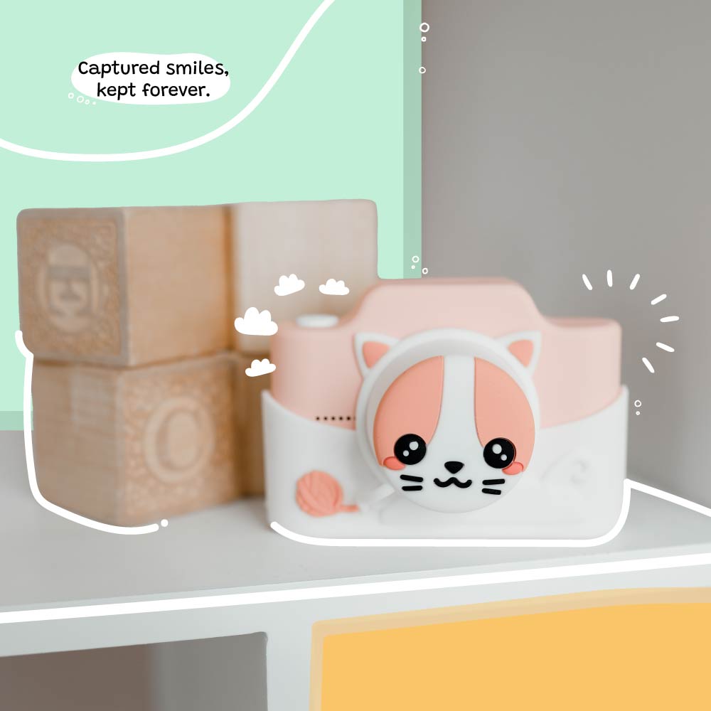 Kidamento Meowie the Cat digital camera with pink silicone cover displayed on a shelf beside wooden toy blocks, capturing a playful and cute design.