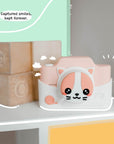 Kidamento Meowie the Cat digital camera with pink silicone cover displayed on a shelf beside wooden toy blocks, capturing a playful and cute design.