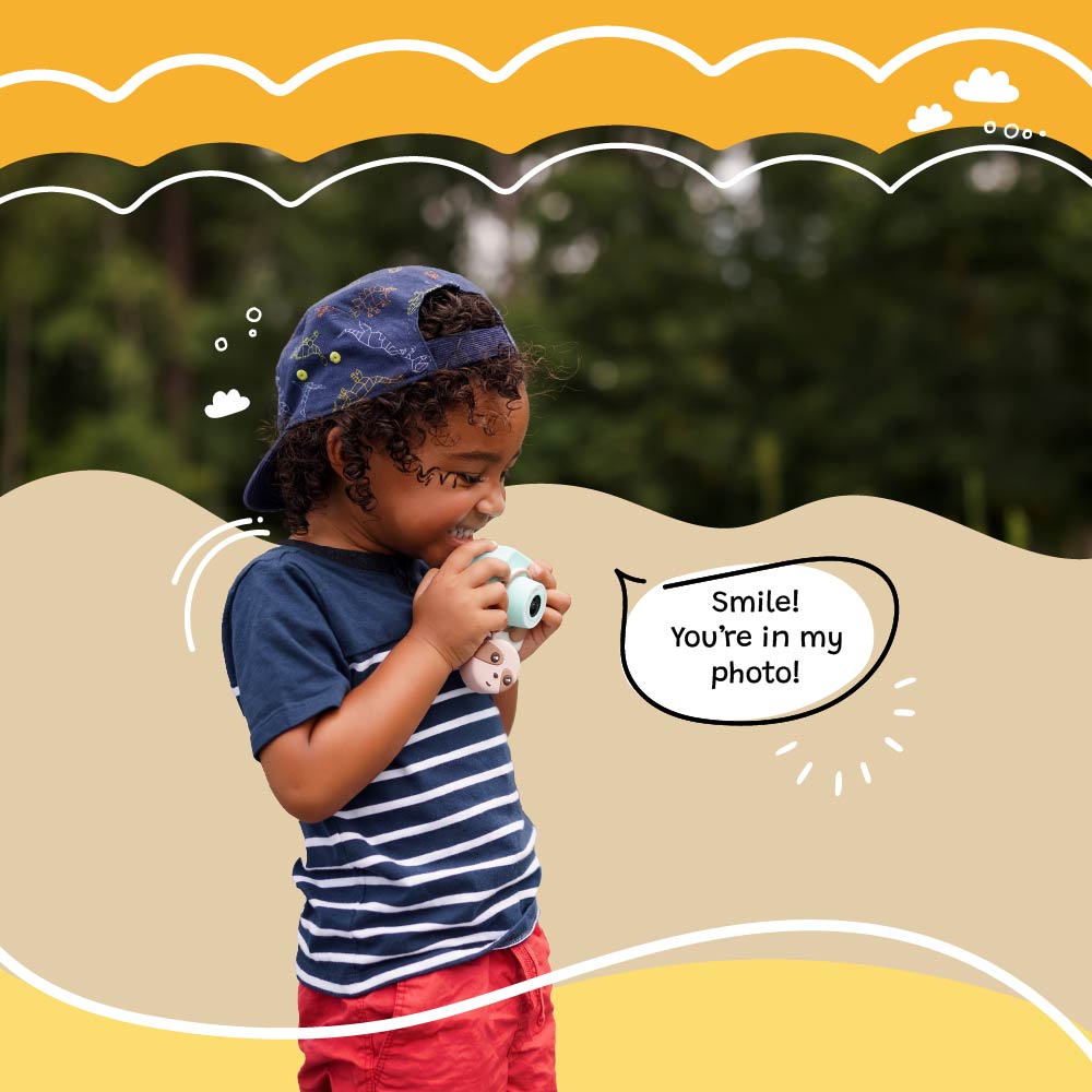 Young boy using Kidamento Model K Zippy the Sloth kids digital camera outdoors, pretending to take a photo with a smile