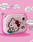 Side angle view of the Kidamento Hello Kitty Model P kids digital camera showing its instant black-and-white thermal print feature. Highlights include cost-effective printing at approximately 5 cents per print, using ink-free, BPA-free, and BPS-free technology. Features Hello Kitty’s face on a pink camera body.