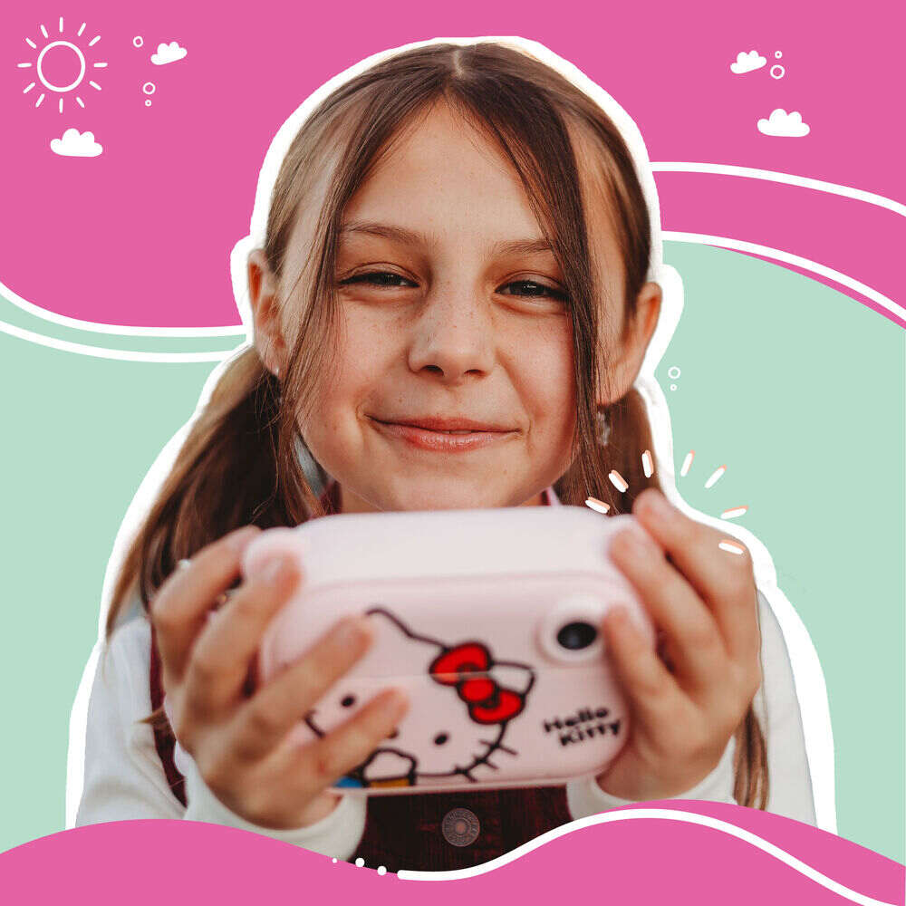 Smiling young girl holding the Kidamento Hello Kitty Model P digital camera, showing joy and excitement. The front of the pastel pink camera with Hello Kitty’s face is clearly visible. The background features playful illustrations in pink, mint green, and white, evoking a cheerful, whimsical atmosphere.