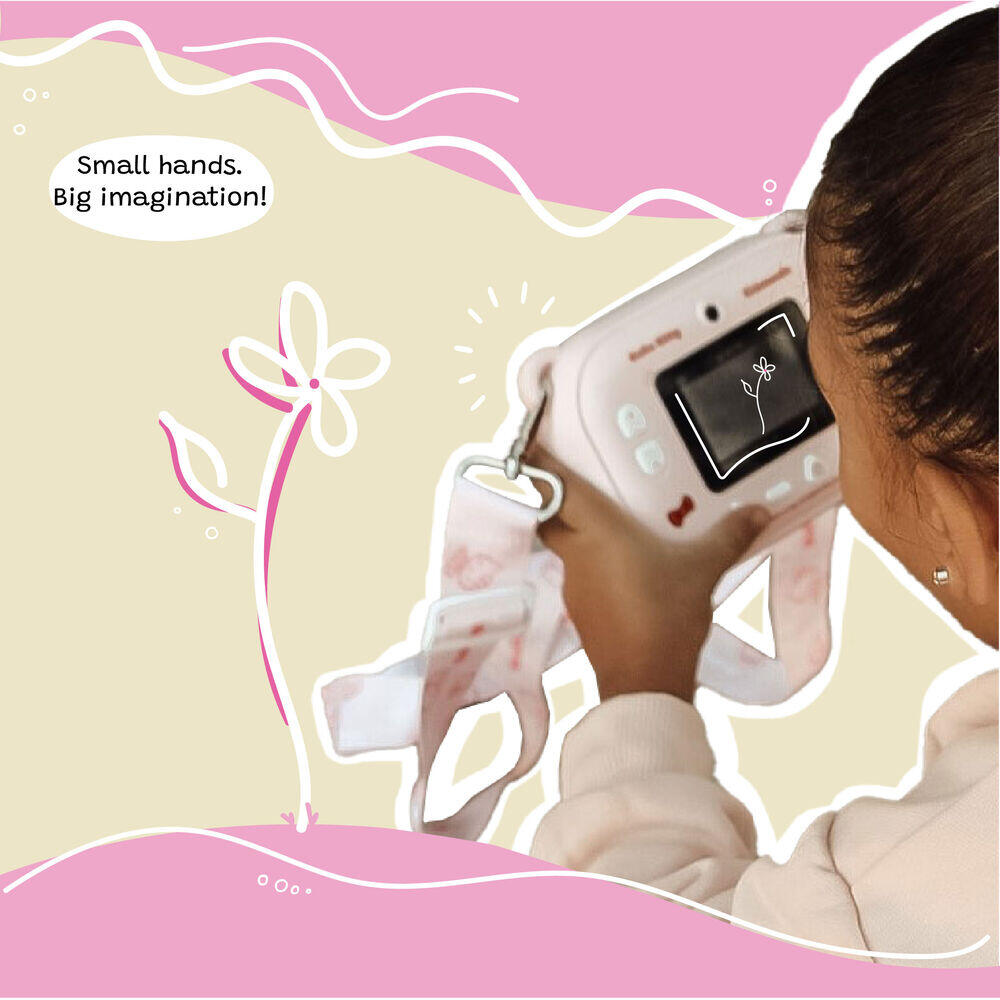 Close-up of a young girl using the Kidamento Hello Kitty Model P camera to take a photo, viewed from behind. The camera screen displays a flower sketch, and the camera strap with Hello Kitty designs hangs around her hands. Caption reads “Small hands. Big imagination!” over a soft pink and beige illustrated background.