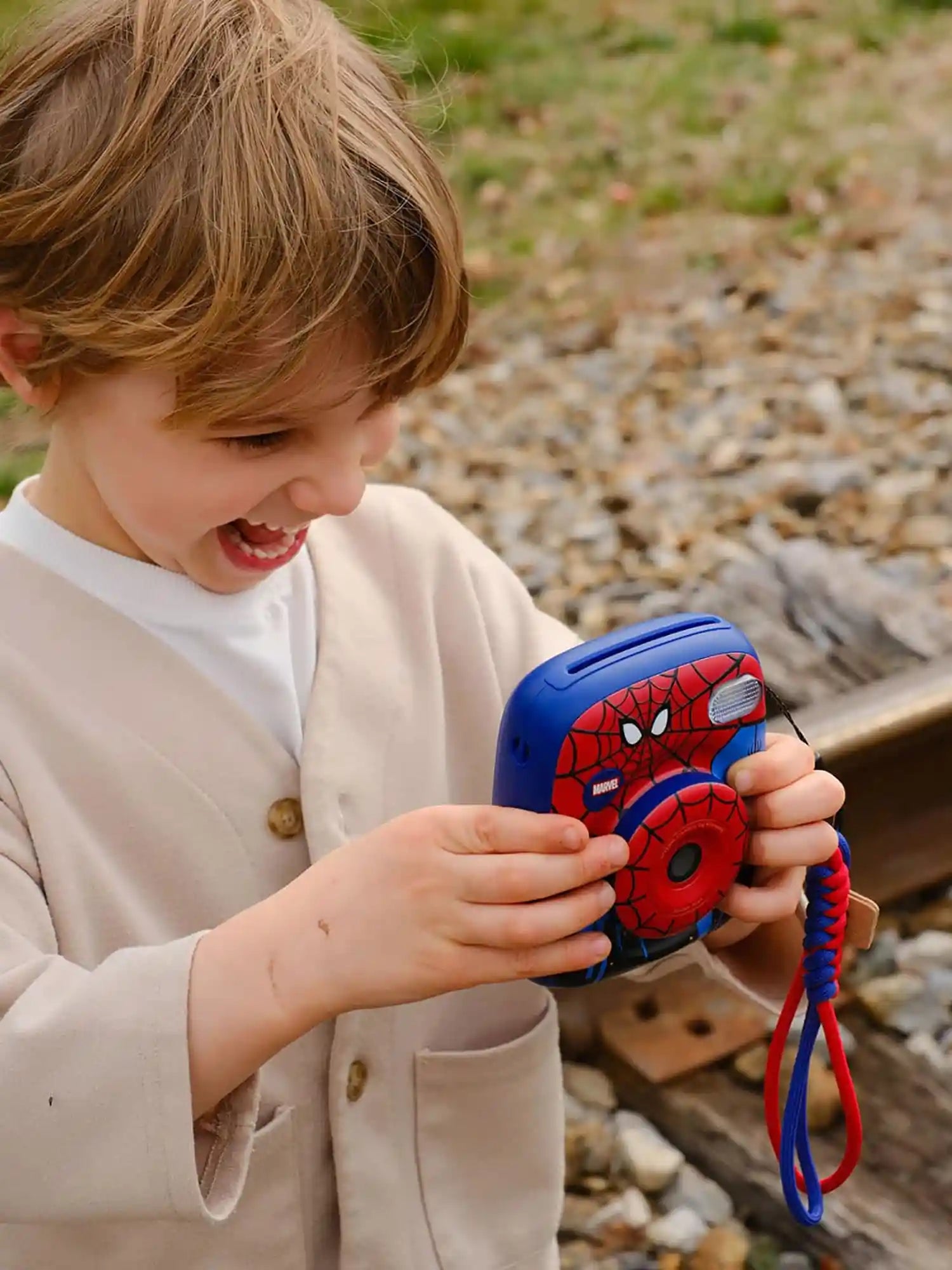 Child holding a toy camera with Spider-Man design outdoors