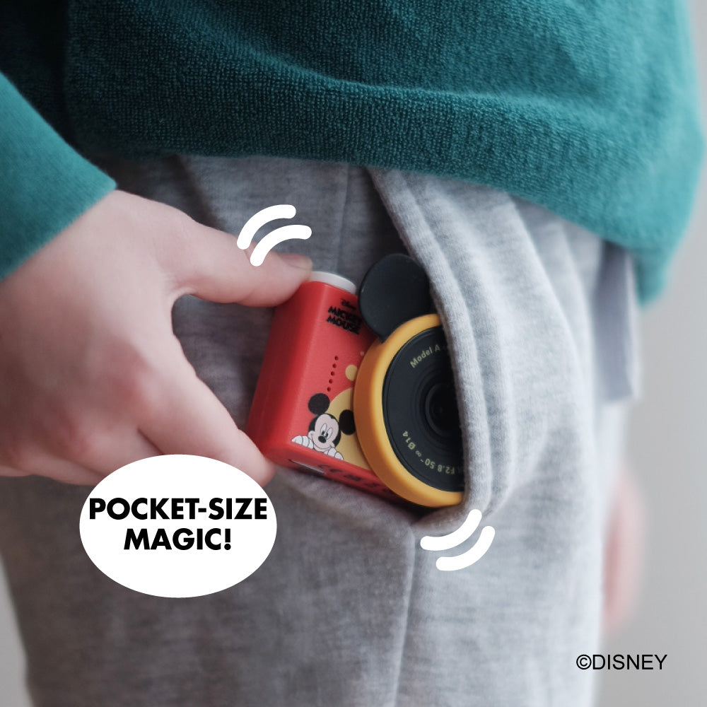 Mickey Mouse mini camera with red body and yellow lens, tucked into a pocket.
