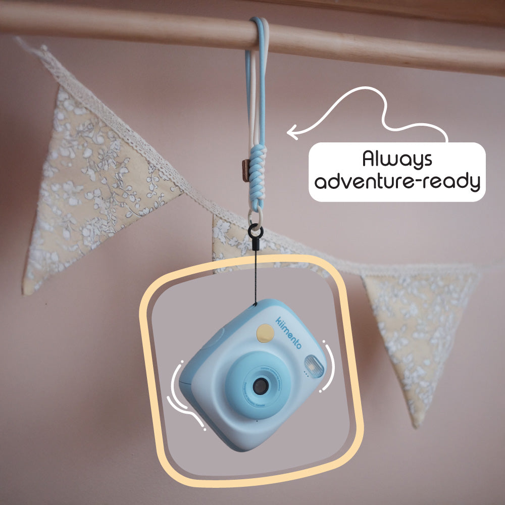 Sky blue instant print camera with a wrist strap hanging from a wooden rod.