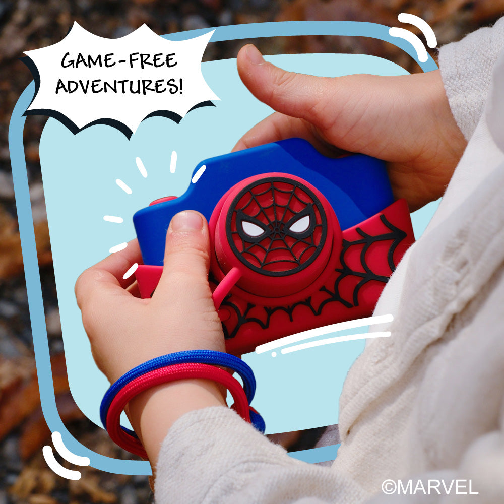 A child's hands hold a blue and red Spider-Man digital camera with a speech bubble that says "GAME-FREE ADVENTURES!".